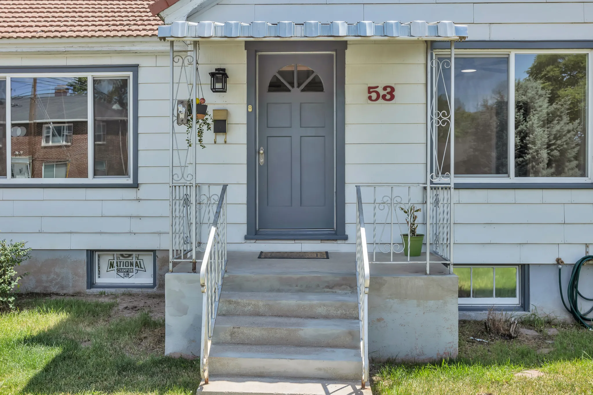 White siding exterior featuring a grey entry door with an arched window insert, concrete steps, and white decorative metal railings