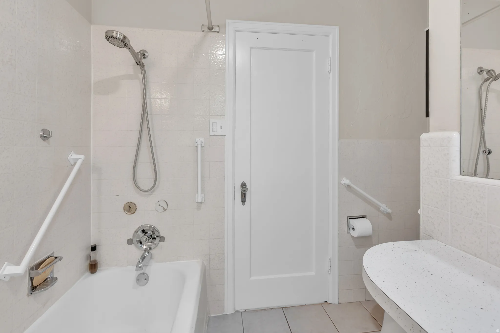 Bathroom featuring a white bathtub with chrome fixtures, a handheld showerhead, and grab bars