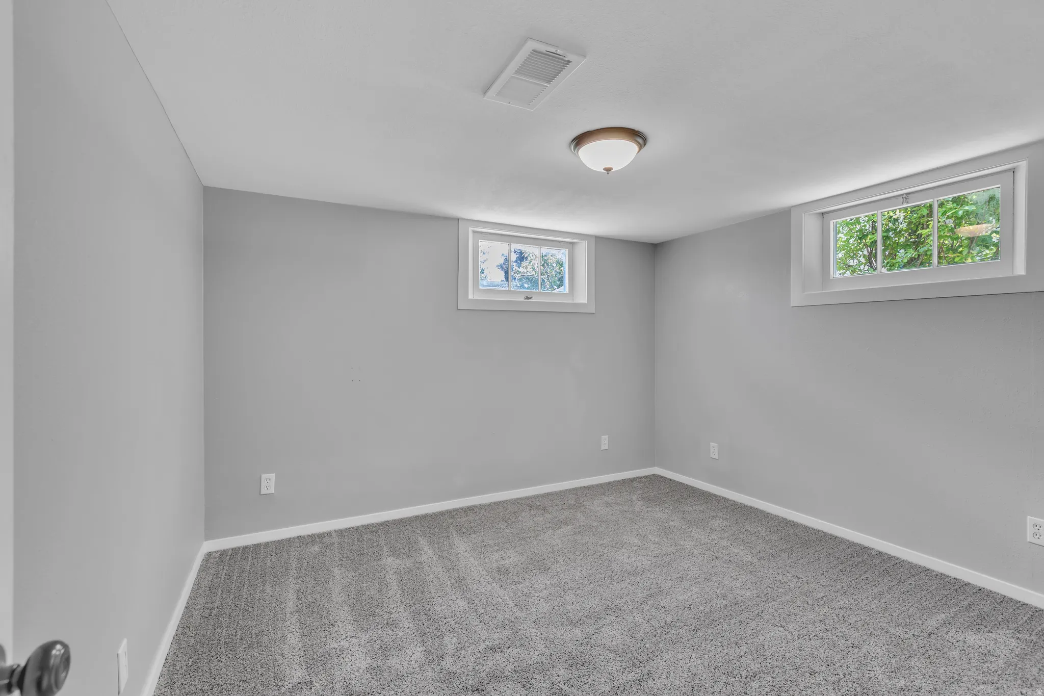 Carpeted room featuring two egress windows, light gray wall paint, white trim, and a ceiling-mounted light fixture