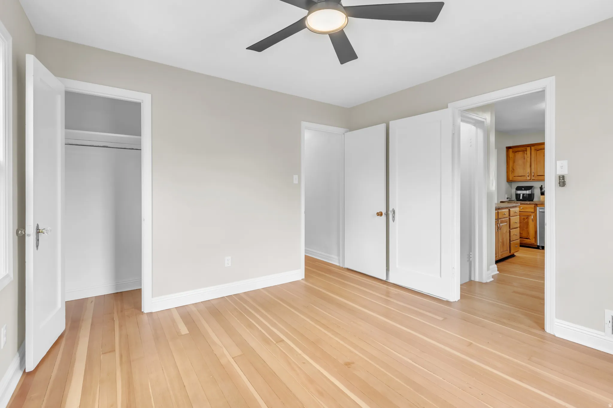 Wood-finish flooring throughout, light-toned wall paint, white trim, and a ceiling fan with integrated lighting