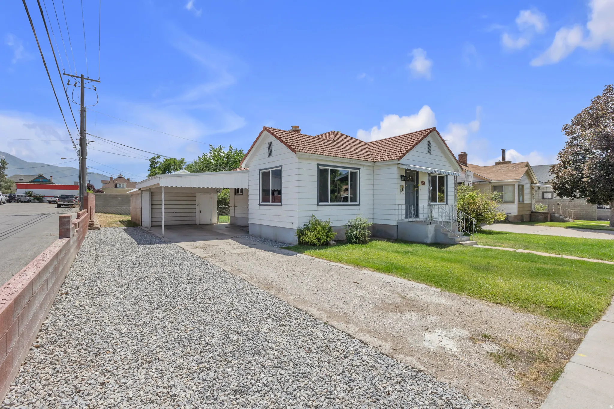 White exterior home with a terracotta roof, featuring a covered carport, gravel side yard, and concrete driveway