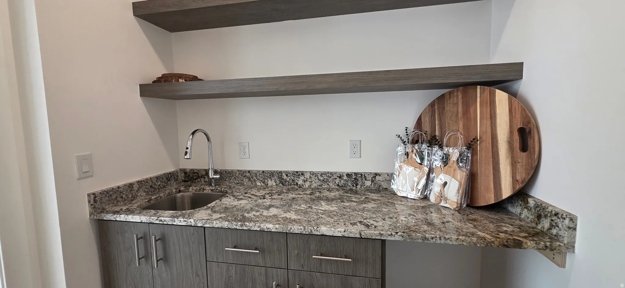 Wet bar featuring a stainless steel sink, gooseneck faucet, and stone-finish countertop