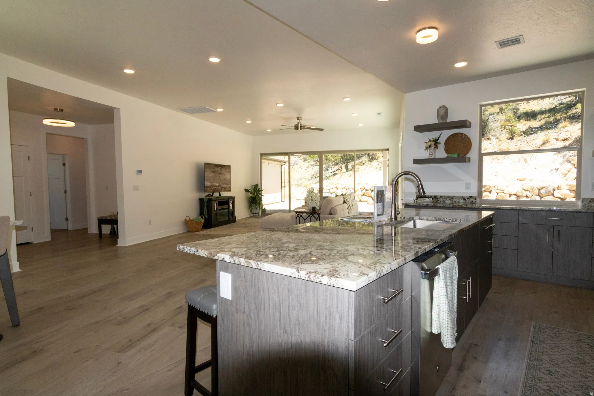 Open-concept kitchen and living area featuring a large island with a stone countertop, coordinating cabinetry, wood-finish flooring, and recessed lighting
