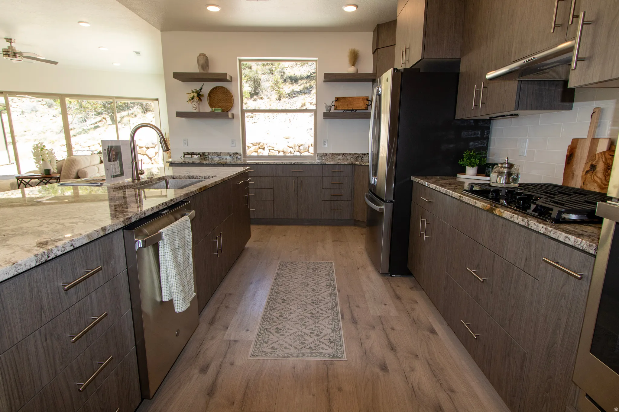 Modern kitchen featuring wood-finish cabinetry, granite countertops, stainless steel appliances, a subway tile backsplash, and wood-finish flooring