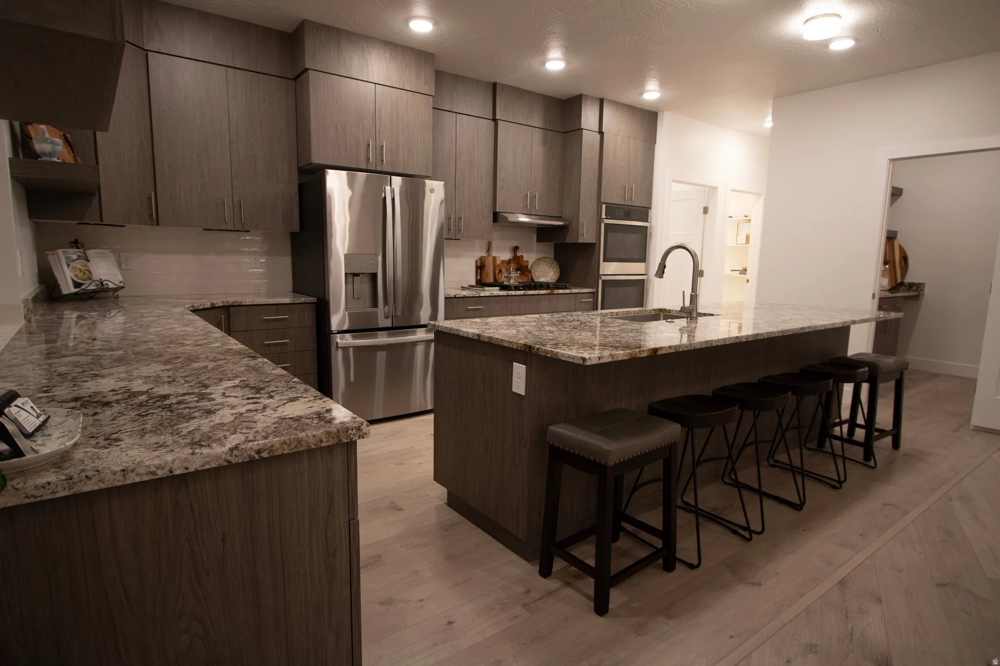 Spacious kitchen featuring an extended island with seating, stainless steel appliances, abundant cabinetry, speckled countertops, and light wood-finish flooring