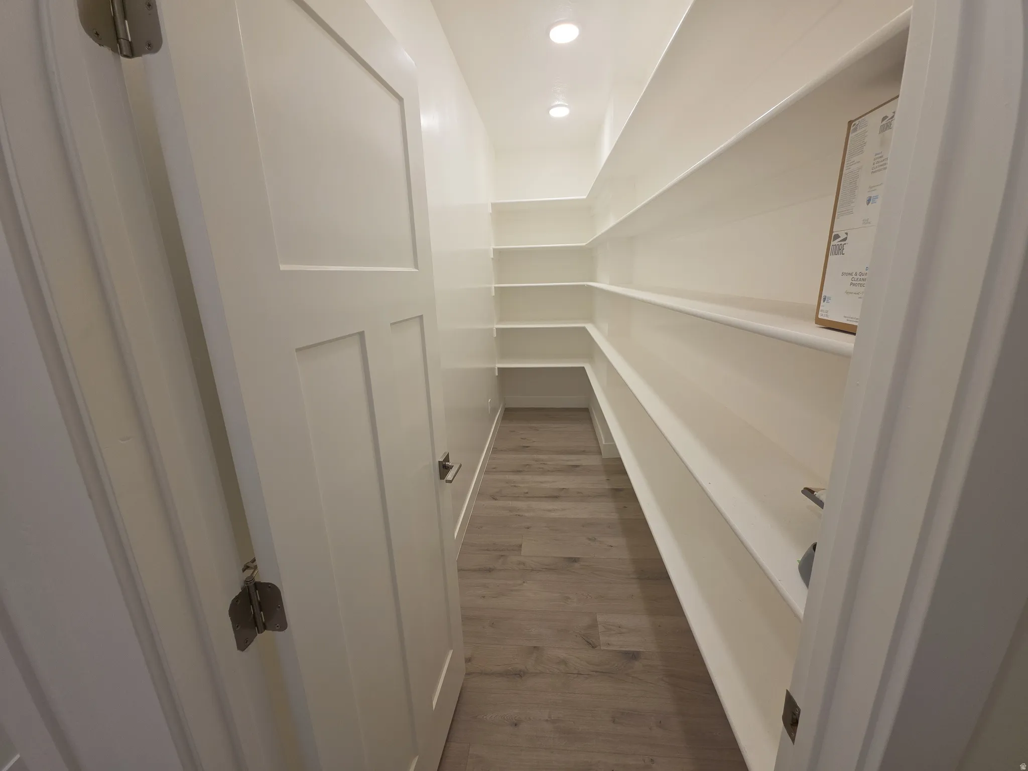 Walk-in pantry featuring extensive built-in shelving, wood-finish flooring, and recessed lighting