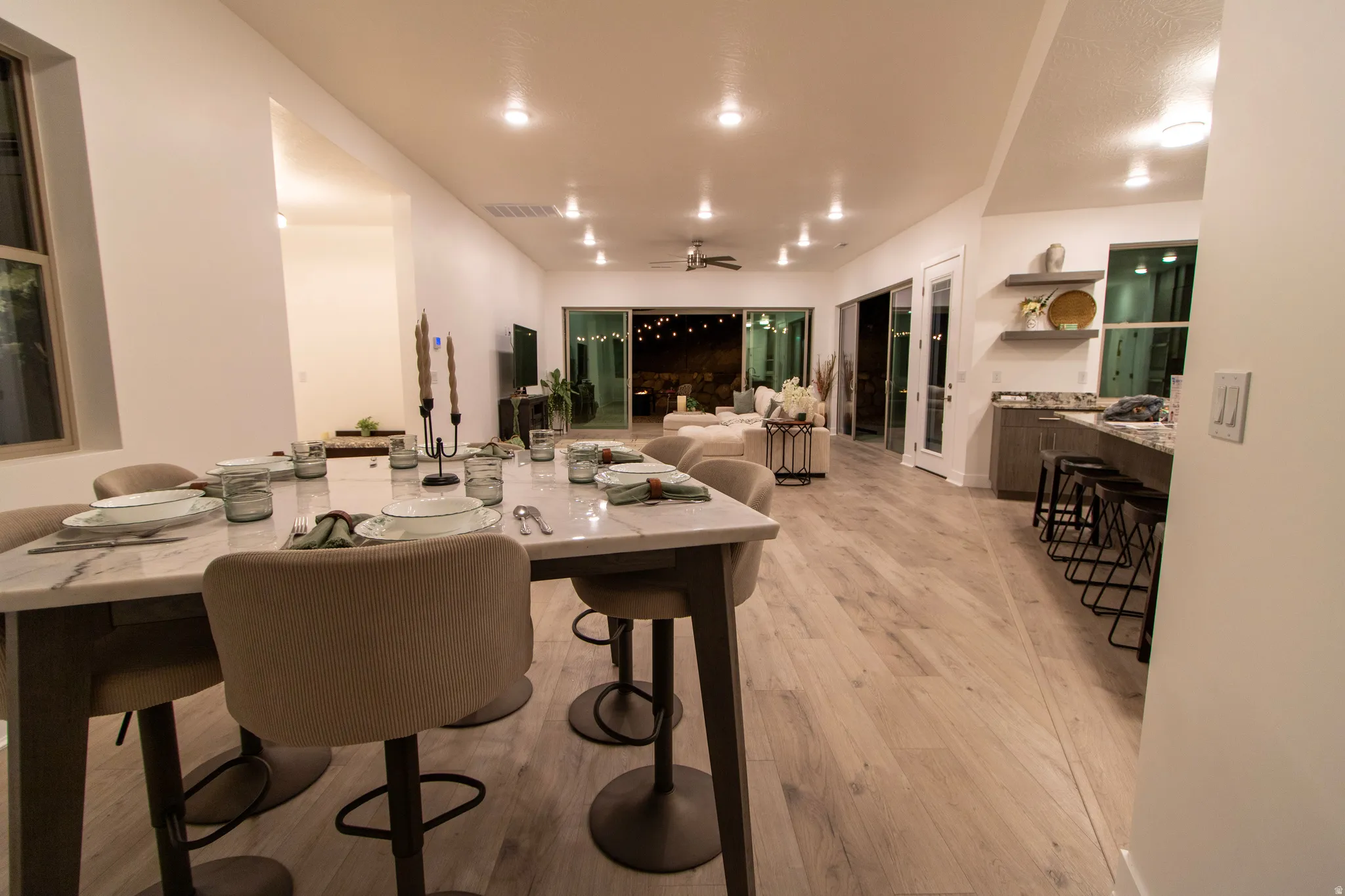 Open-concept living space featuring wood-finish flooring, a dining area with a marble-finish table, recessed lighting, and sliding glass doors leading to an outdoor area