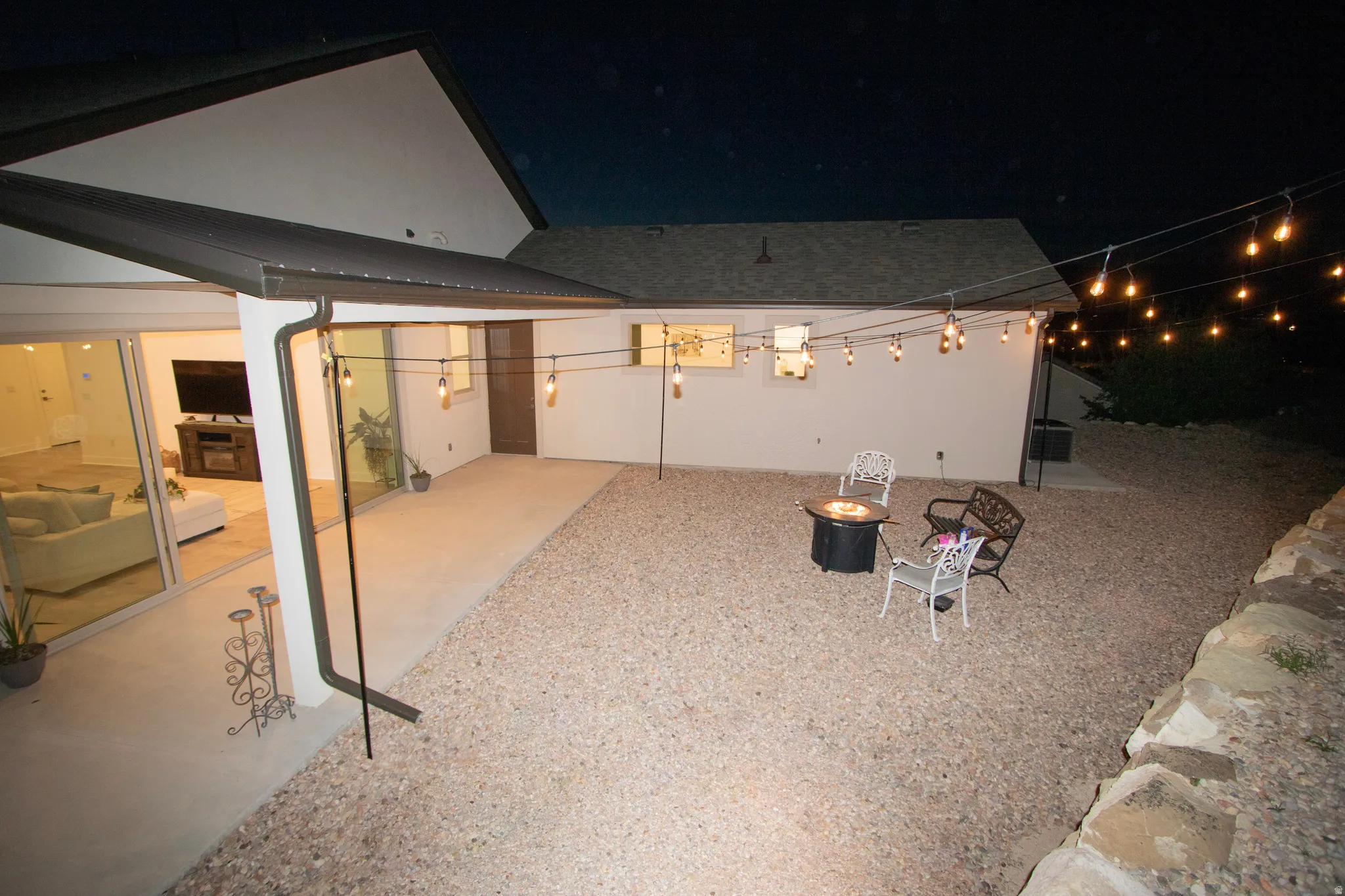 Expansive outdoor area featuring a gravel ground cover, a built-in fire pit, string lighting, and a covered concrete patio