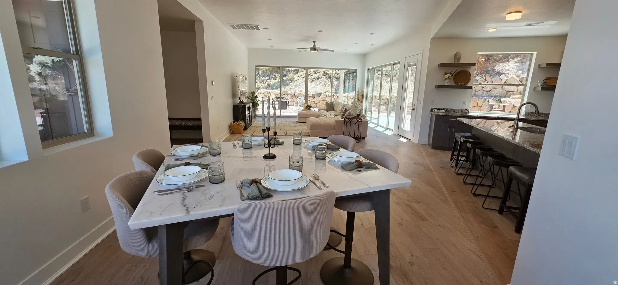 Open-concept interior featuring wood-finish flooring, a contemporary dining table with a stone-look surface, and a kitchen island with a dark stone countertop