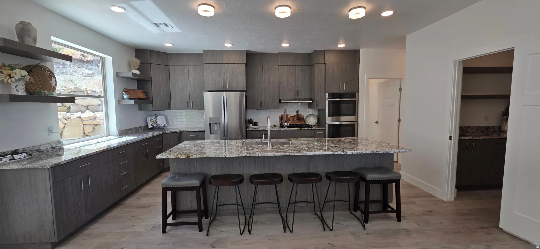 Spacious kitchen featuring an expansive island with stone countertops, gray cabinetry, stainless steel appliances, and light wood-finish flooring