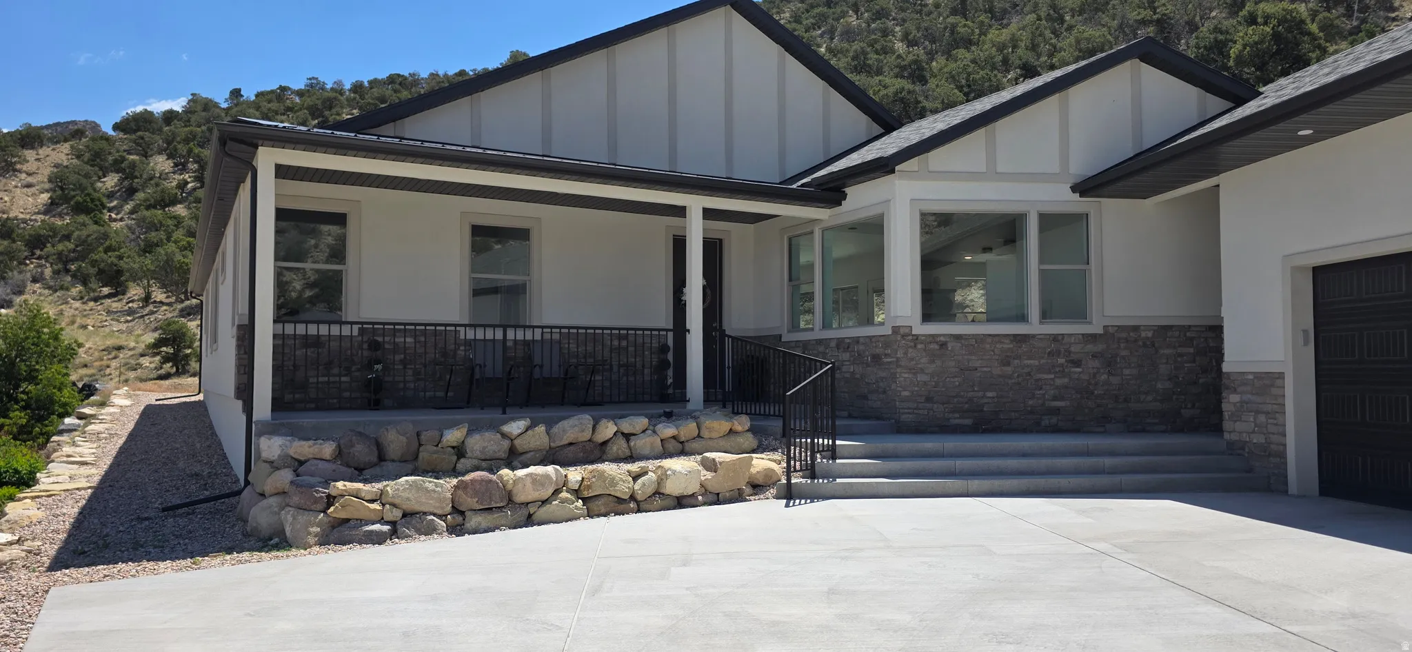 Contemporary exterior featuring a covered front porch with black metal railings, a board and batten facade, and stone veneer accents