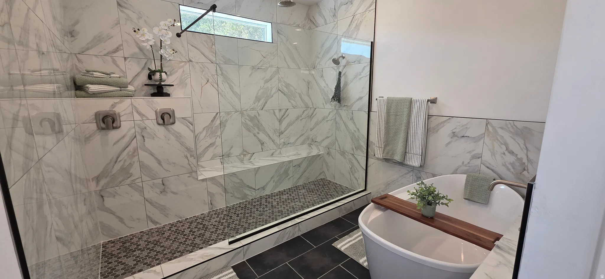 Spacious bathroom featuring a frameless glass shower enclosure with a built-in bench, a rain shower head, and a mosaic tile floor