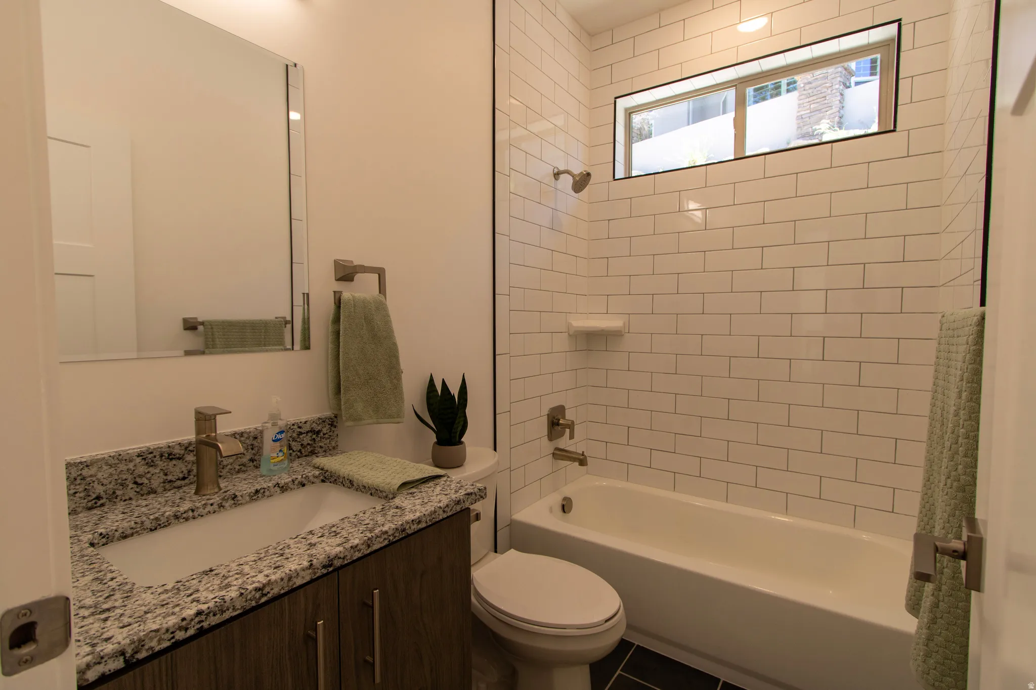 Full bathroom featuring a tub/shower combination with subway tile surround, an elongated transom window, a dark wood-finish vanity with a granite countertop, and a rectangular undermount sink