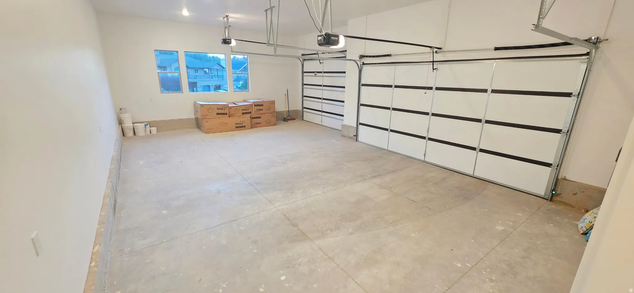 Spacious garage featuring a concrete floor, three large windows, two overhead garage doors, and two garage door openers