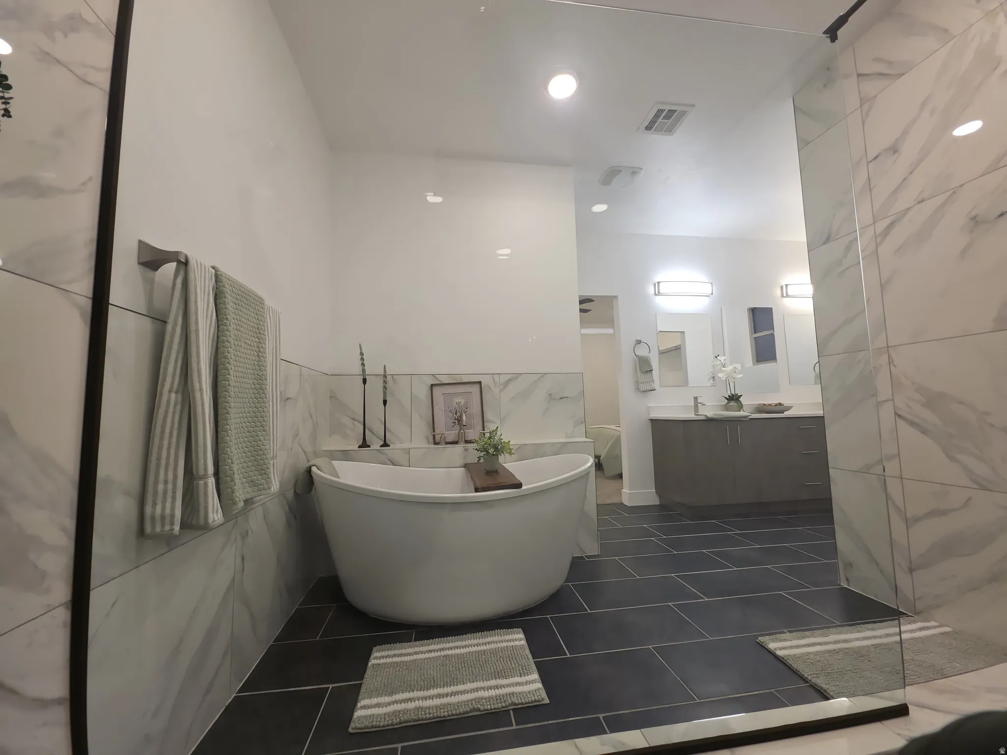 Spacious bathroom featuring a freestanding soaking tub, large format tile flooring, and marble-look wall tiles
