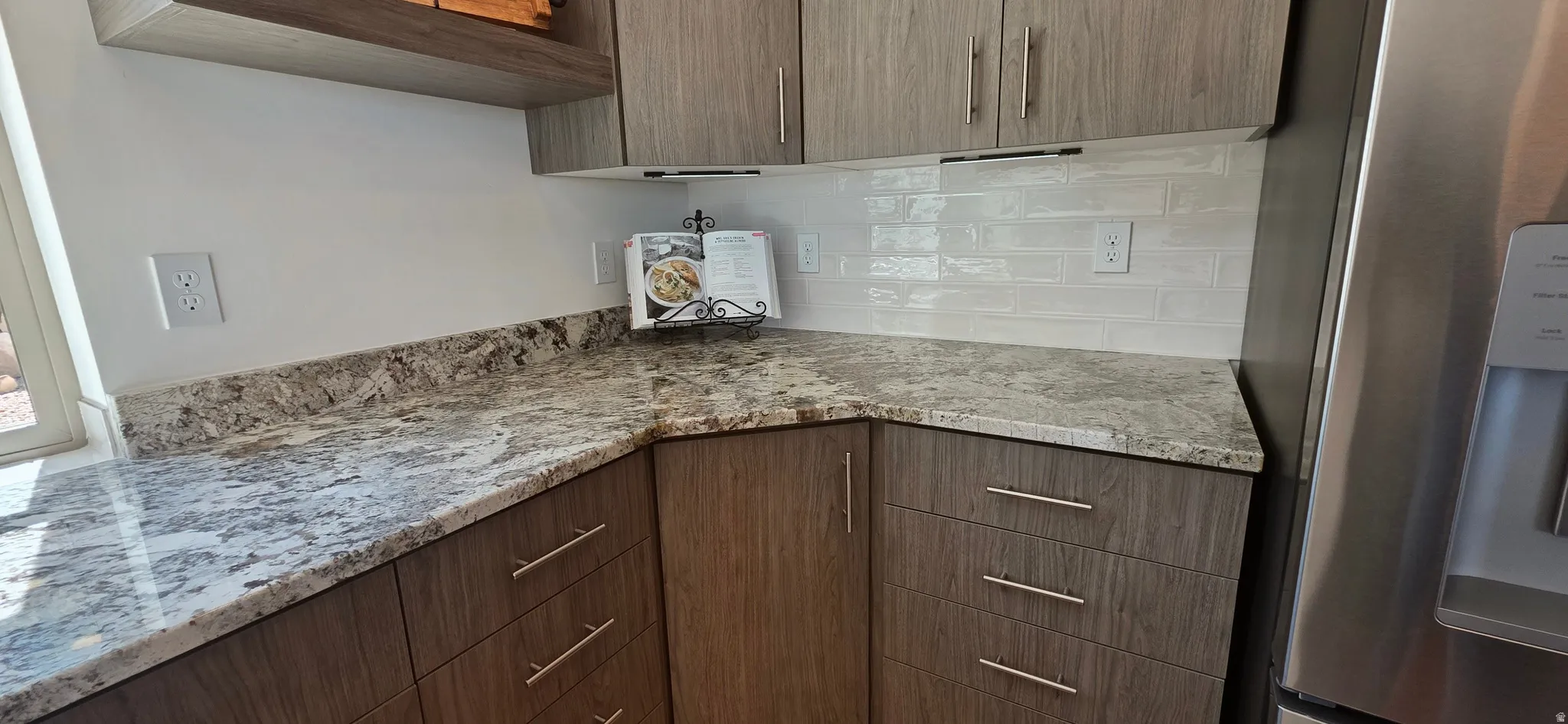Kitchen corner featuring granite countertops, wood-finish cabinetry with brushed nickel hardware, and a white subway tile backsplash