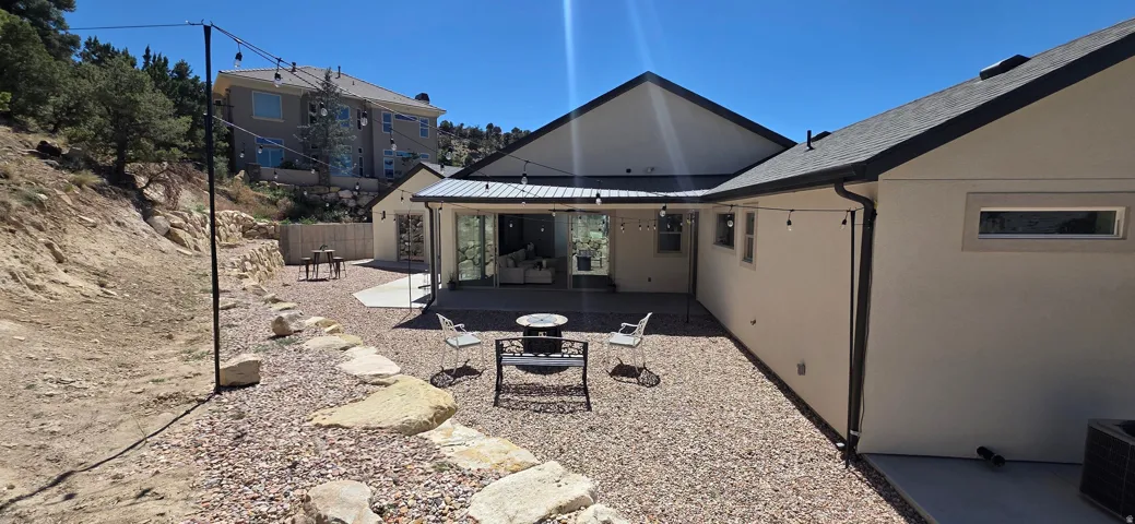 Expansive gravel patio area featuring a concrete entertainment space, sliding glass doors, and string lighting