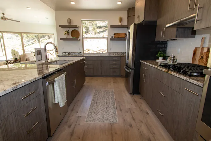 Modern kitchen featuring wood-finish cabinetry, granite countertops, stainless steel appliances, a subway tile backsplash, and wood-finish flooring