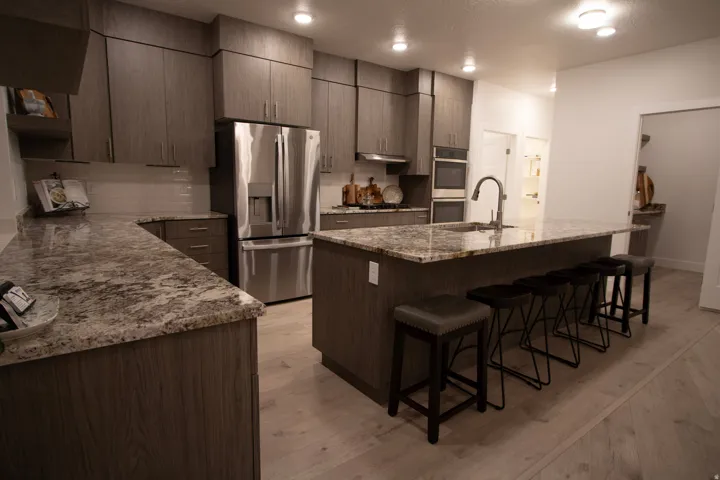 Spacious kitchen featuring an extended island with seating, stainless steel appliances, abundant cabinetry, speckled countertops, and light wood-finish flooring