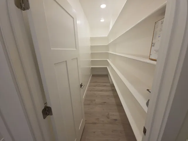 Walk-in pantry featuring extensive built-in shelving, wood-finish flooring, and recessed lighting