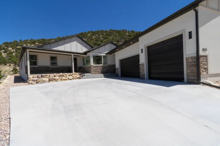 Exterior with a concrete driveway, stone accents, and a covered porch with a metal railing
