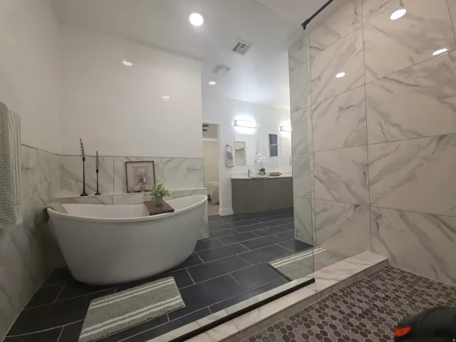 Spacious bathroom featuring a freestanding soaking tub, large format tile shower, dual vanity with undermount sinks, and contrasting floor tiles