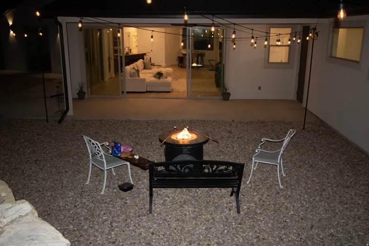 Expansive gravel patio with a built-in fire pit, string lighting, and a concrete paver area