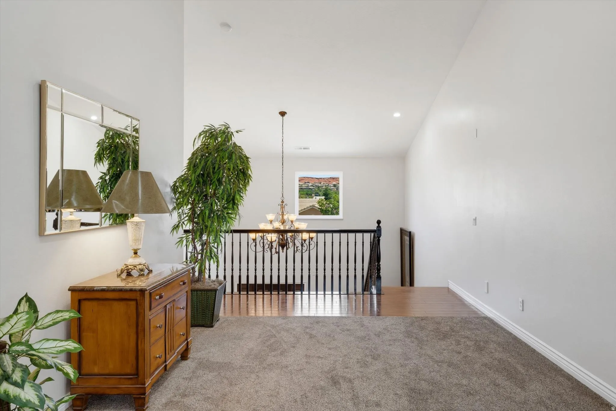 Upper-level landing featuring a chandelier, black spindle railing, a window with distant scenery, and mixed flooring with carpeting and wood-finish