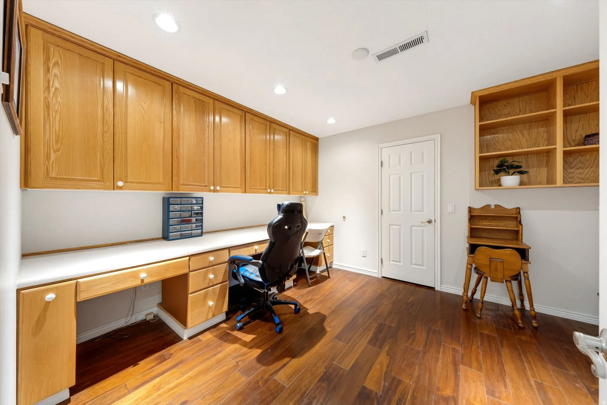 Dedicated room featuring extensive built-in cabinetry, long white countertops, recessed lighting, wood-finish flooring, and a six-panel interior door