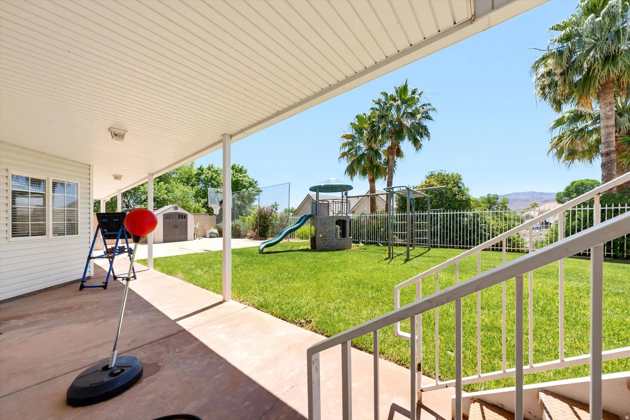 Expansive covered patio with concrete flooring, white metal railings, and dual exterior lights