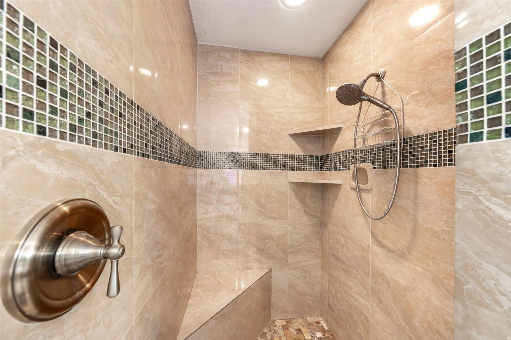 Tiled shower featuring a built-in bench, dual recessed shelves, a handheld showerhead, and mosaic accent tiling