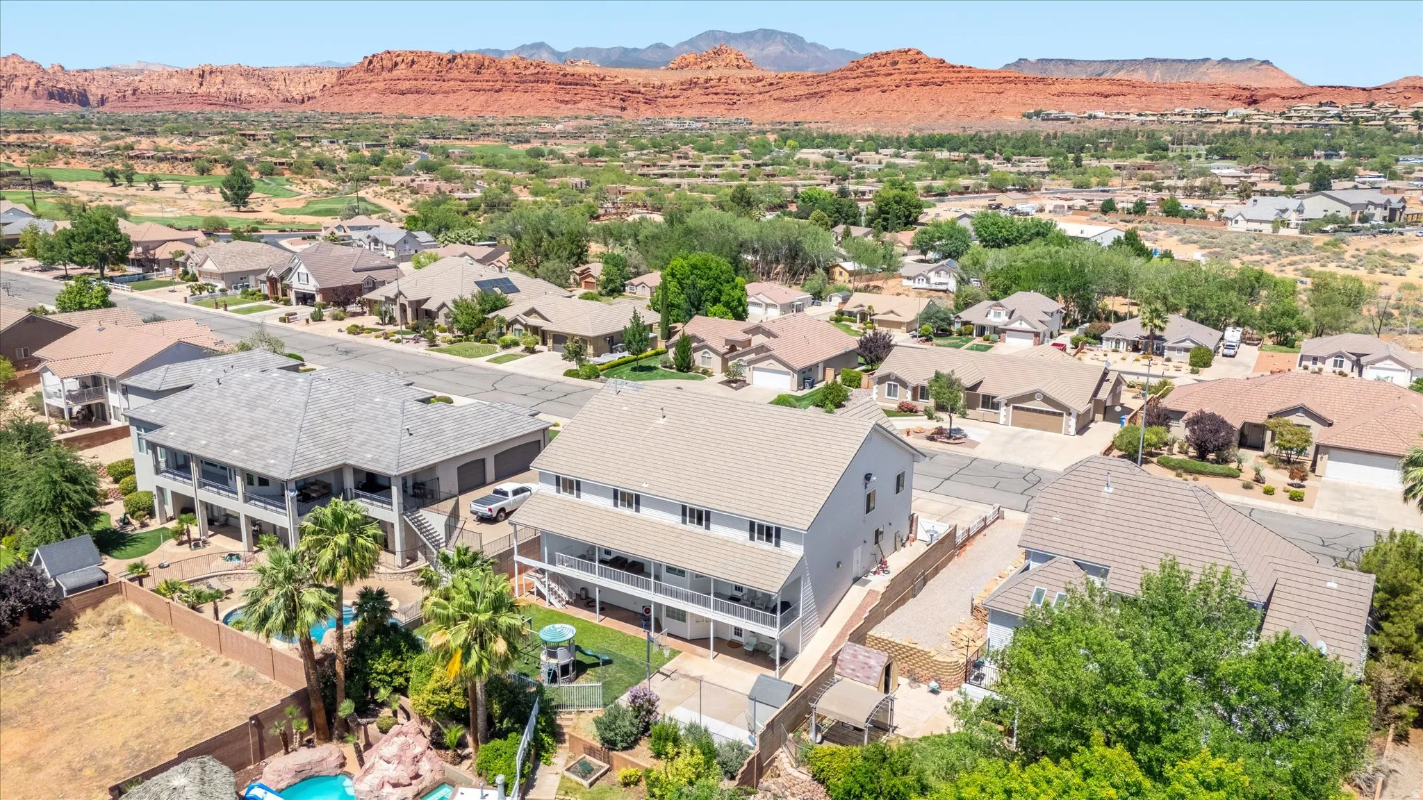 Aerial property view showcasing a multi-story residence with a covered lower-level patio, surrounded by mature trees