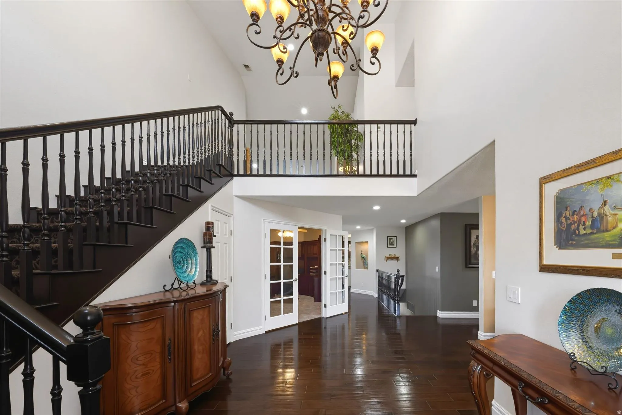 Entryway featuring a grand staircase with dark wood-finish treads and balusters, a second-story landing with matching railing, and a large chandelier
