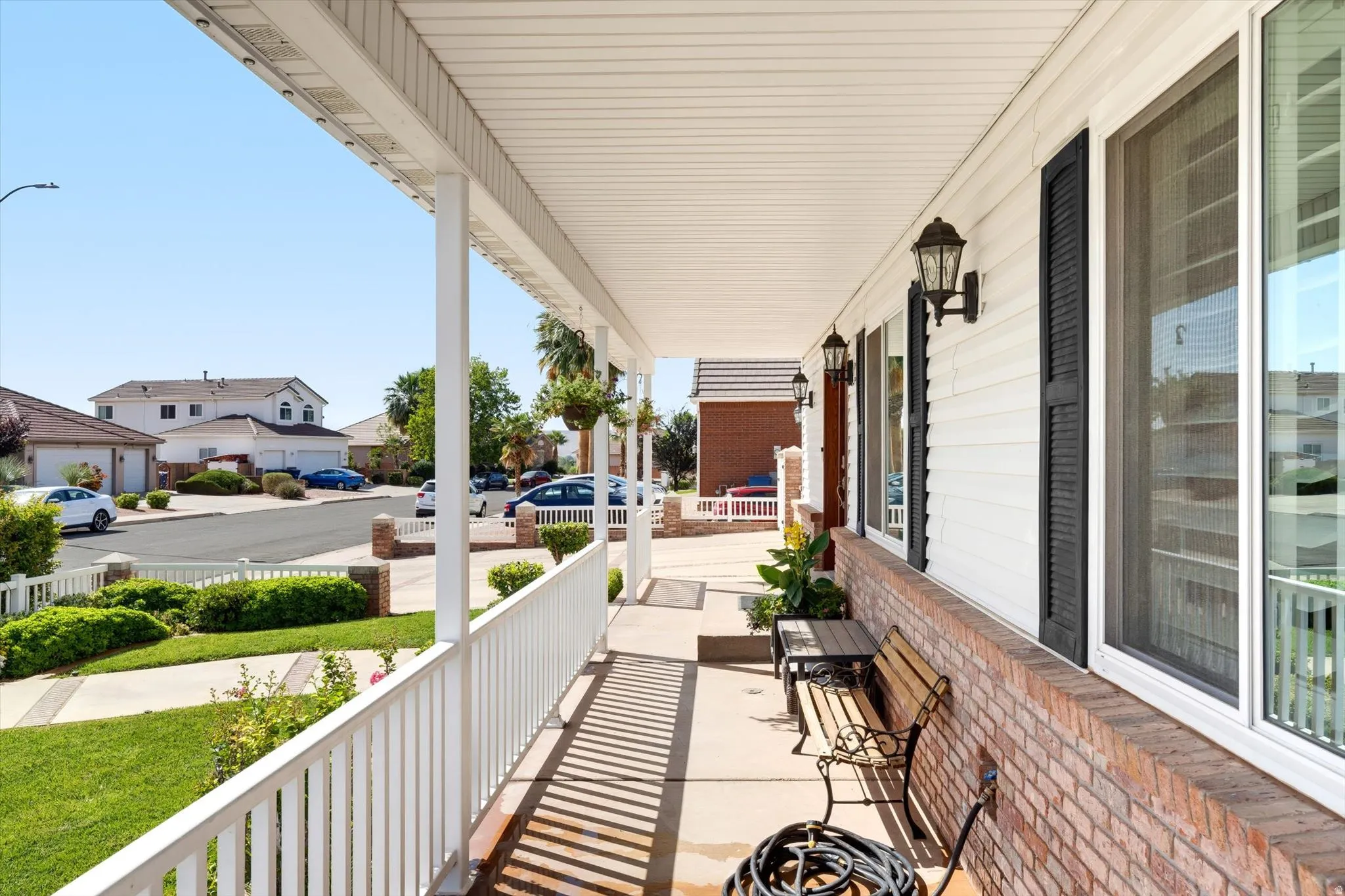 Inviting covered front porch with white siding, brick foundation, and multiple windows featuring black shutters