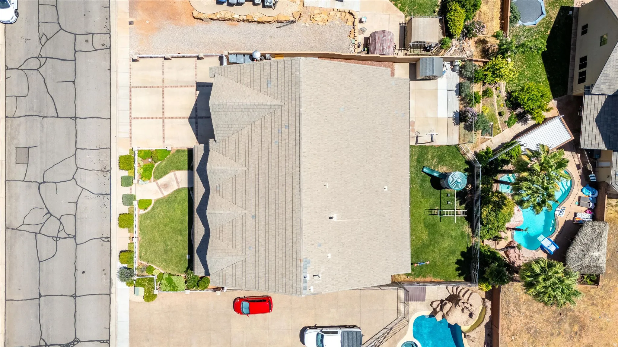 Expansive property featuring a multi-level roofline, extensive paved driveways, a manicured front lawn, a large backyard with a grassy area, and a private swimming pool with rock features and mature palm trees