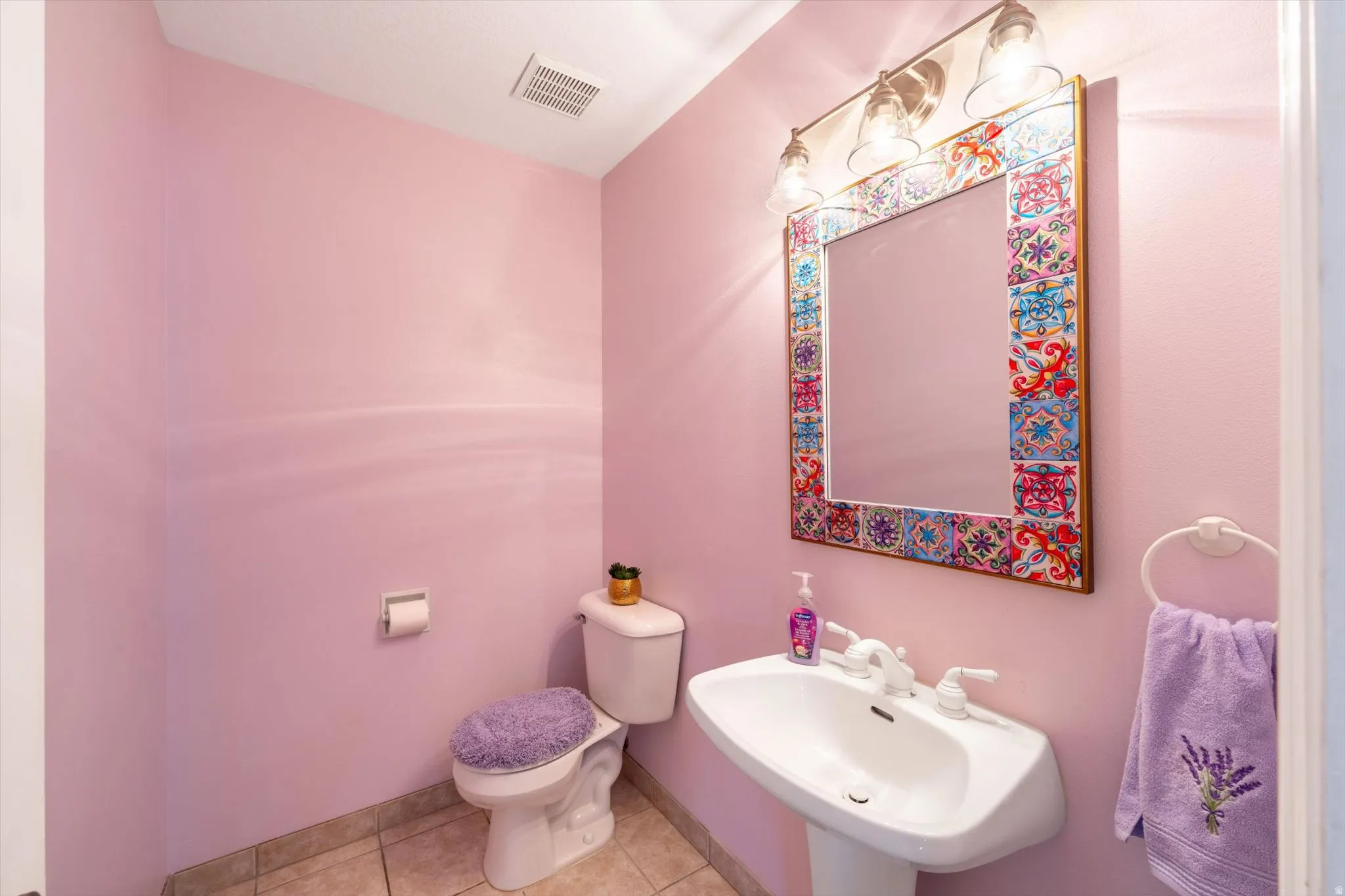 Powder room featuring a pedestal sink, ceramic tile flooring, and a decorative mirror with a tiled frame