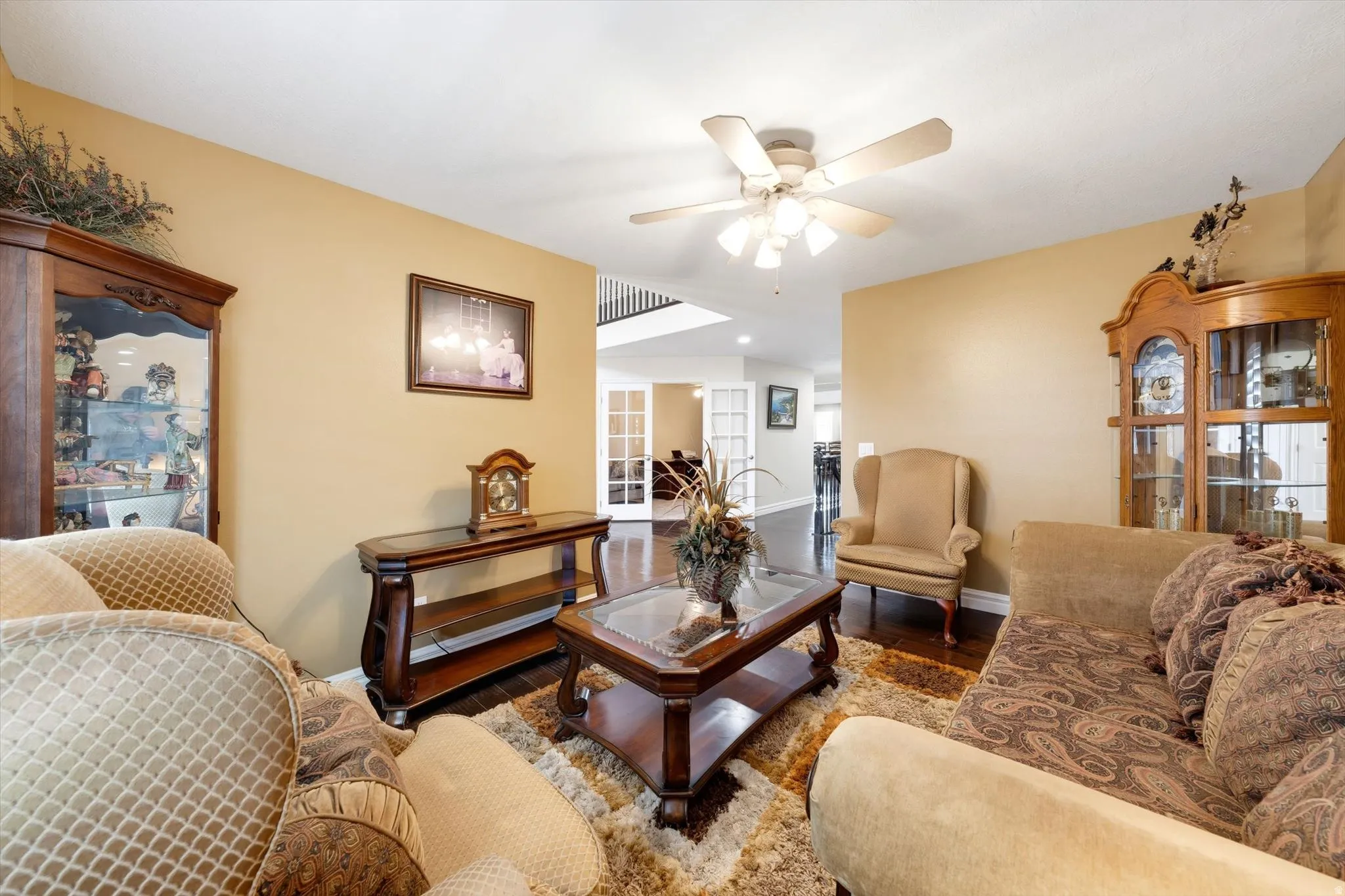 Spacious living room featuring wood-finish flooring, a ceiling fan with integrated lighting, and warm neutral wall tones