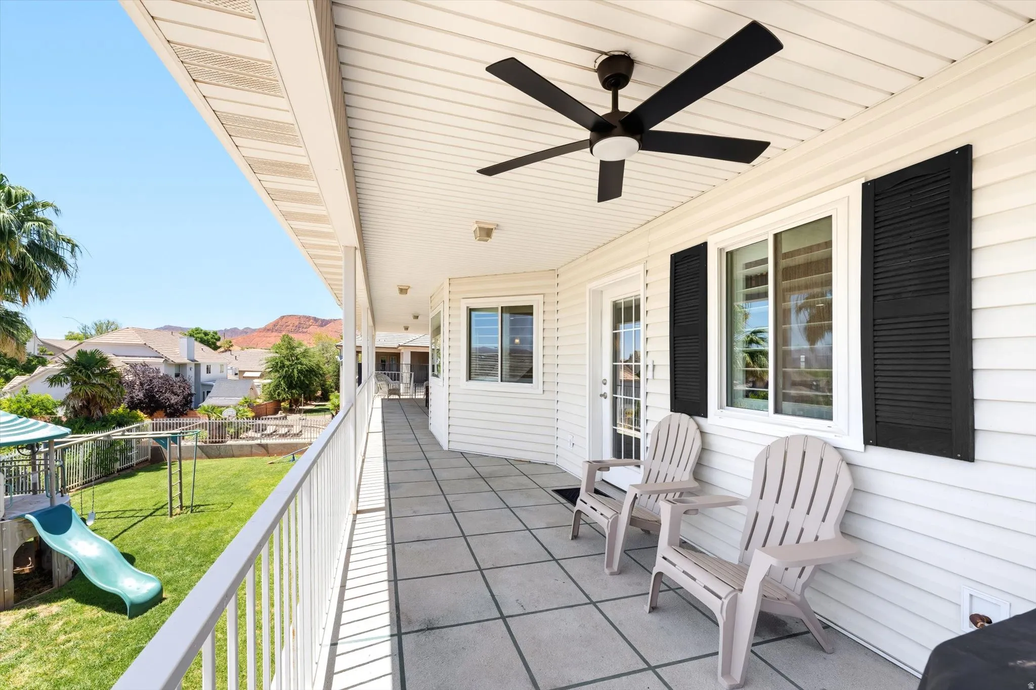 Covered patio featuring a ceiling fan, white siding, black louvered shutters, and square tile flooring