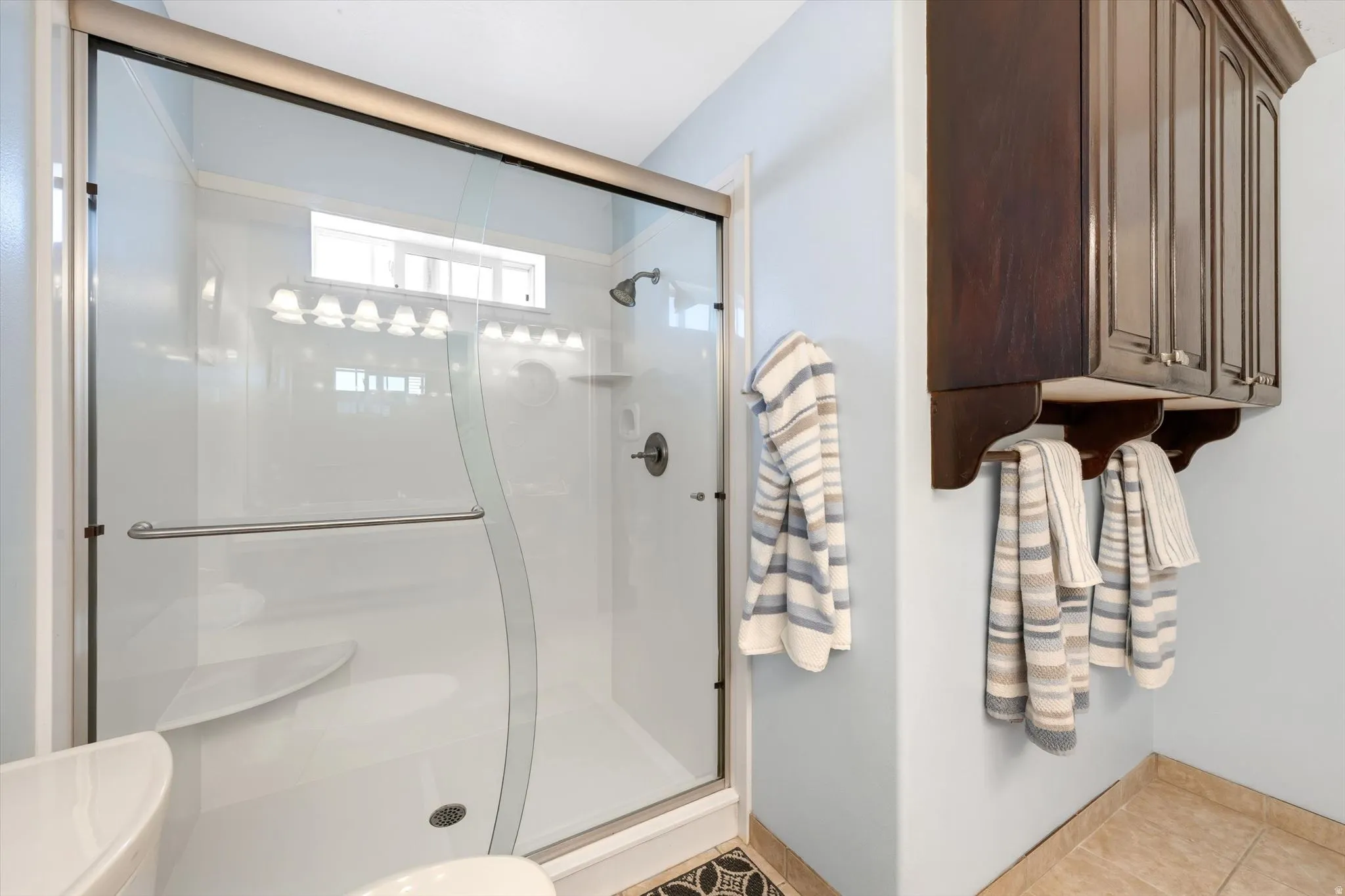 Enclosed shower with glass door and built-in seating, featuring a transom window and wall-mounted lighting
