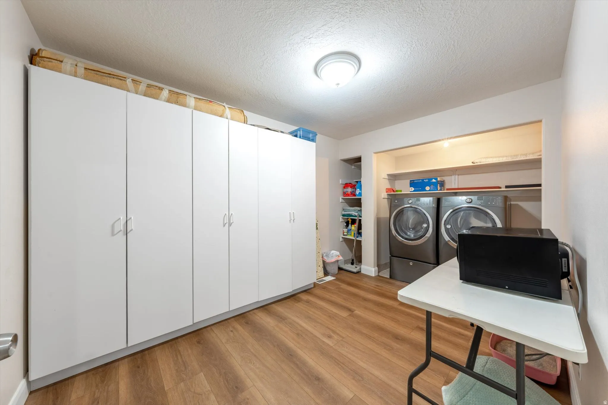 Dedicated laundry area featuring a built-in appliance alcove with overhead shelving, extensive full-height cabinetry, and wood-finish flooring