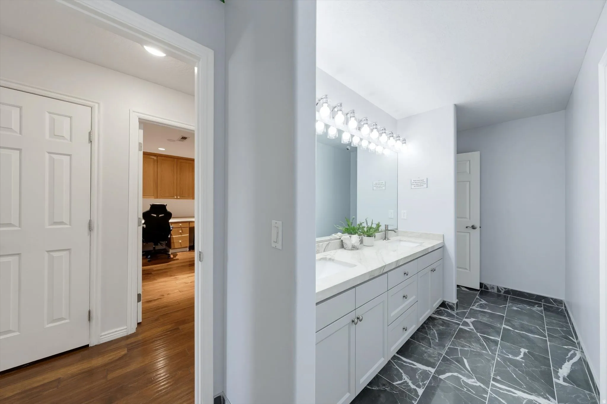 Bathroom featuring a dual vanity with light grey cabinetry, a light-toned countertop, and dark patterned tile flooring