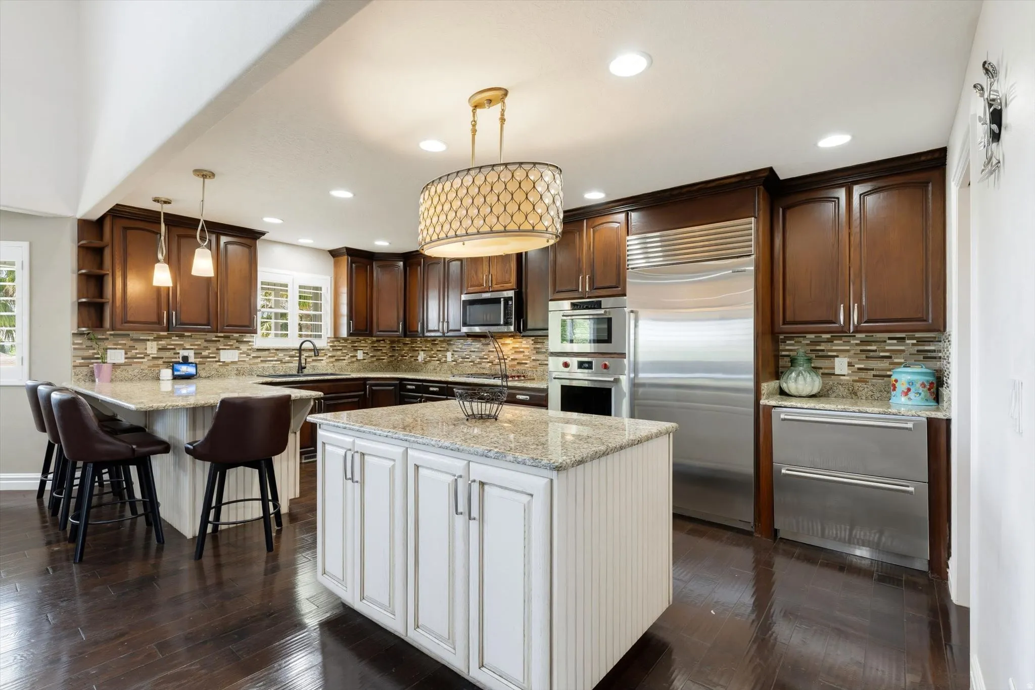 Gourmet kitchen featuring dark wood-finish flooring, a central island with a light-toned countertop, dark wood cabinetry, stainless steel appliances, and a tiled backsplash