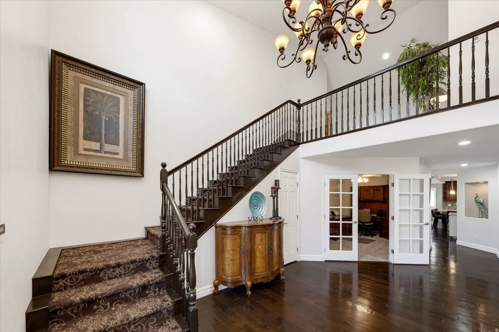 Two-story foyer featuring dark wood-finish flooring, a grand staircase with patterned carpet runner, and a wrought iron chandelier