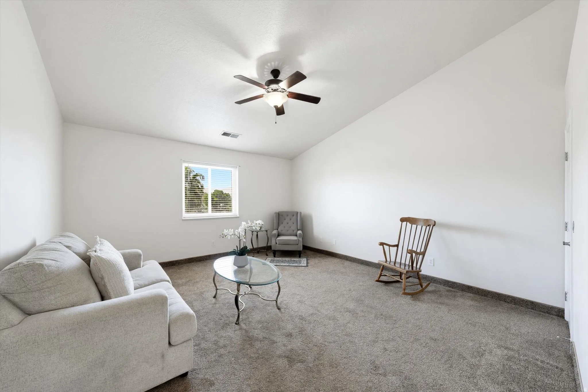 Spacious room featuring vaulted ceilings, neutral-toned carpeting, a window with blinds, and a ceiling fan with integrated lighting