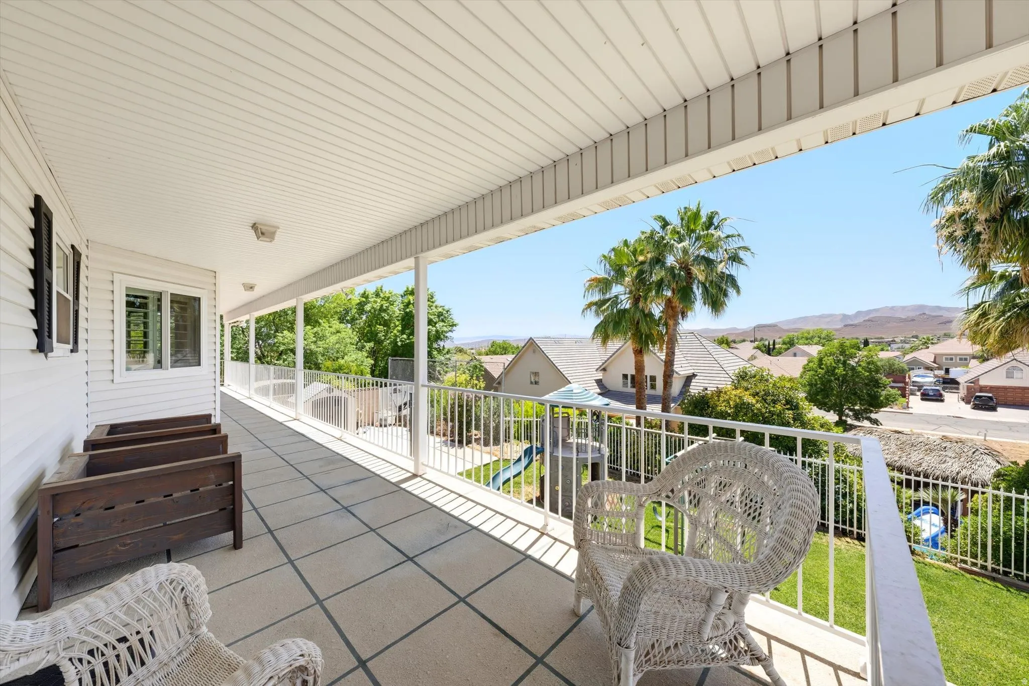 Expansive covered balcony featuring a tile-patterned floor, white railing, and exterior siding with black shutters