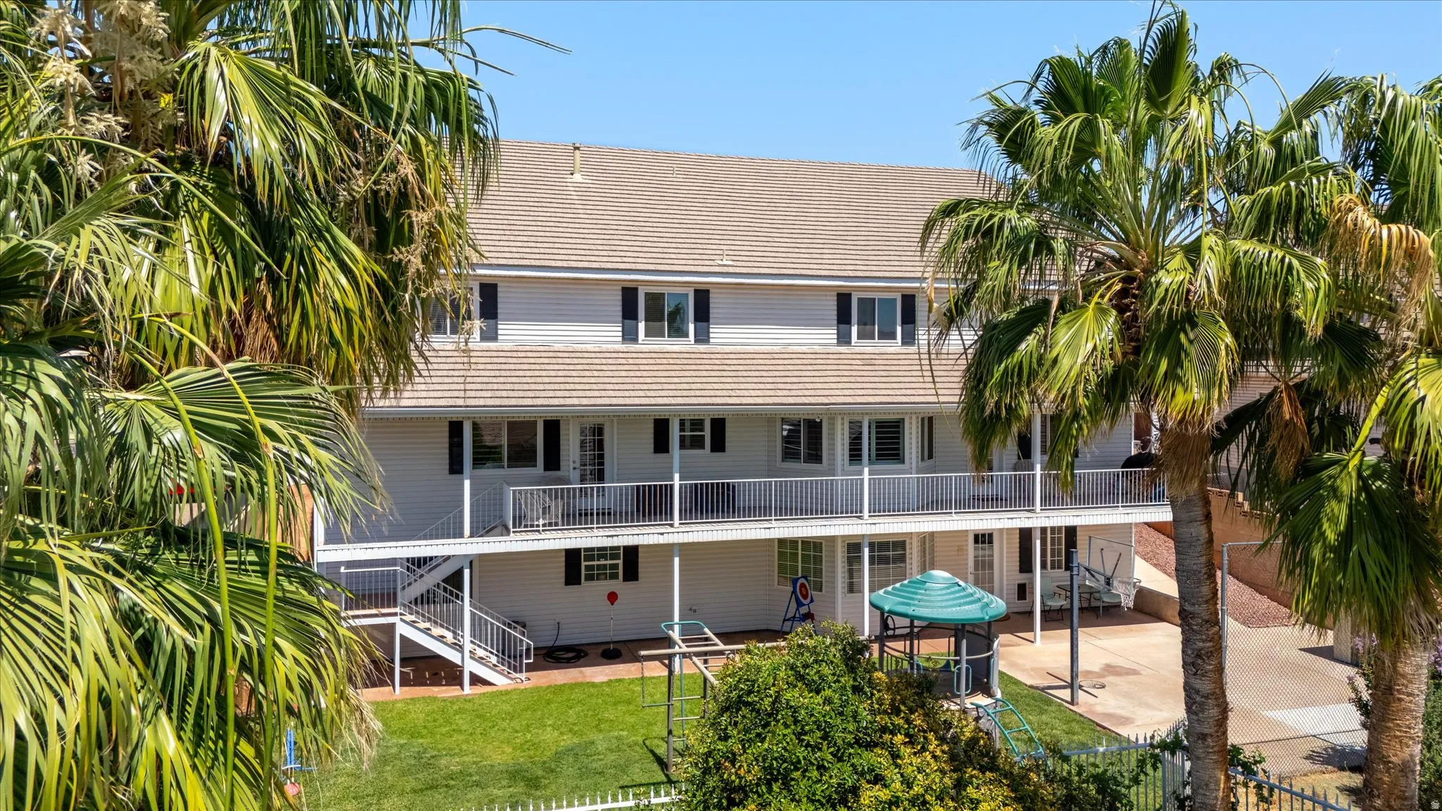 Multi-story residence featuring a ground-level patio with a green awning, a tiered upper-level balcony with white railings, and a manicured lawn