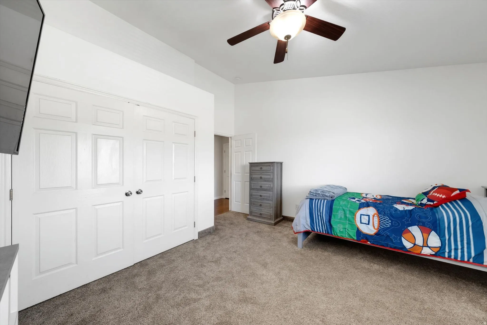 Spacious room featuring neutral carpeting, a four-panel closet with white doors and brushed nickel hardware, and a ceiling fan with integrated lighting