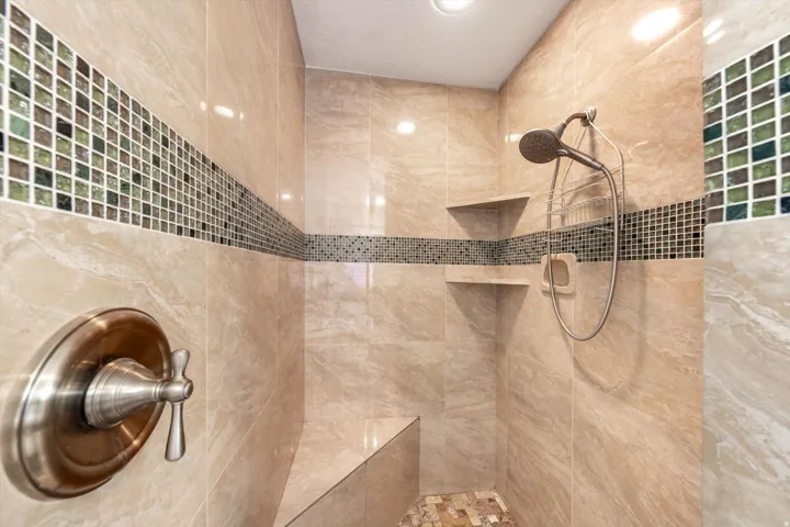 Tiled shower featuring a built-in bench, dual recessed shelves, a handheld showerhead, and mosaic accent tiling