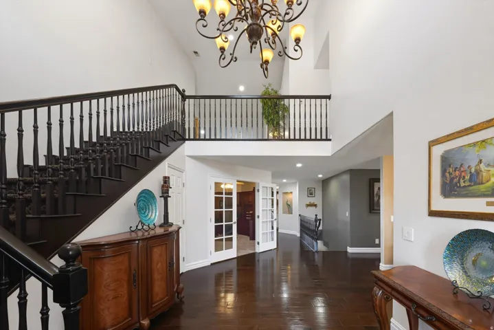 Entryway featuring a grand staircase with dark wood-finish treads and balusters, a second-story landing with matching railing, and a large chandelier