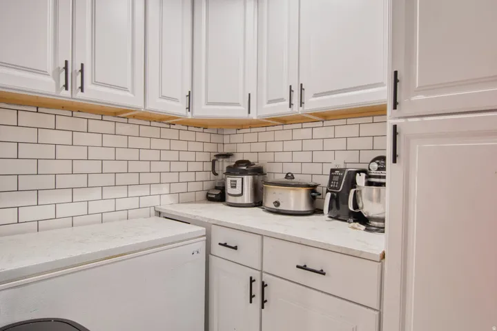 White shaker-style cabinetry with black hardware, white subway tile backsplash with dark grout, and light-toned countertops